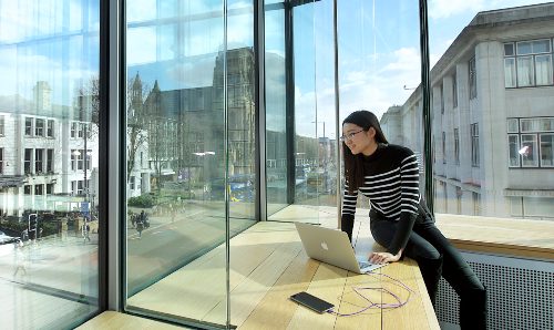 A student looks at a laptop while looking over the University campus.