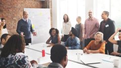 A group of people standing and sitting around a table during a workshop. 